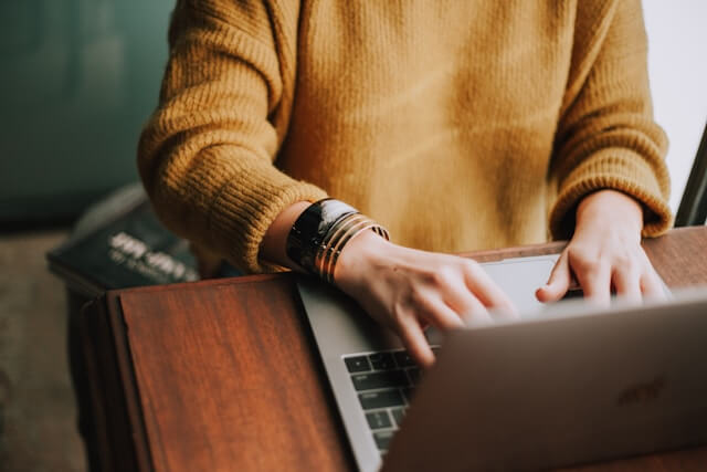 Woman in a sweater typing on a laptop computer